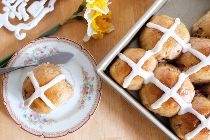Tray of Chai and cherry hot crossed buns next to a plate with a single bun.