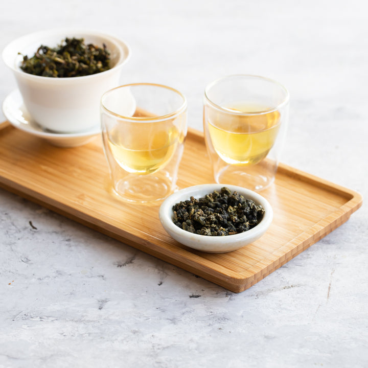 Wooden tray with bowl of loose tea, two gaiwan cups of brewed tea and gaiwan of wet tea leaves.