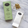Green box next to bundle of paper tea filters on a marble background.