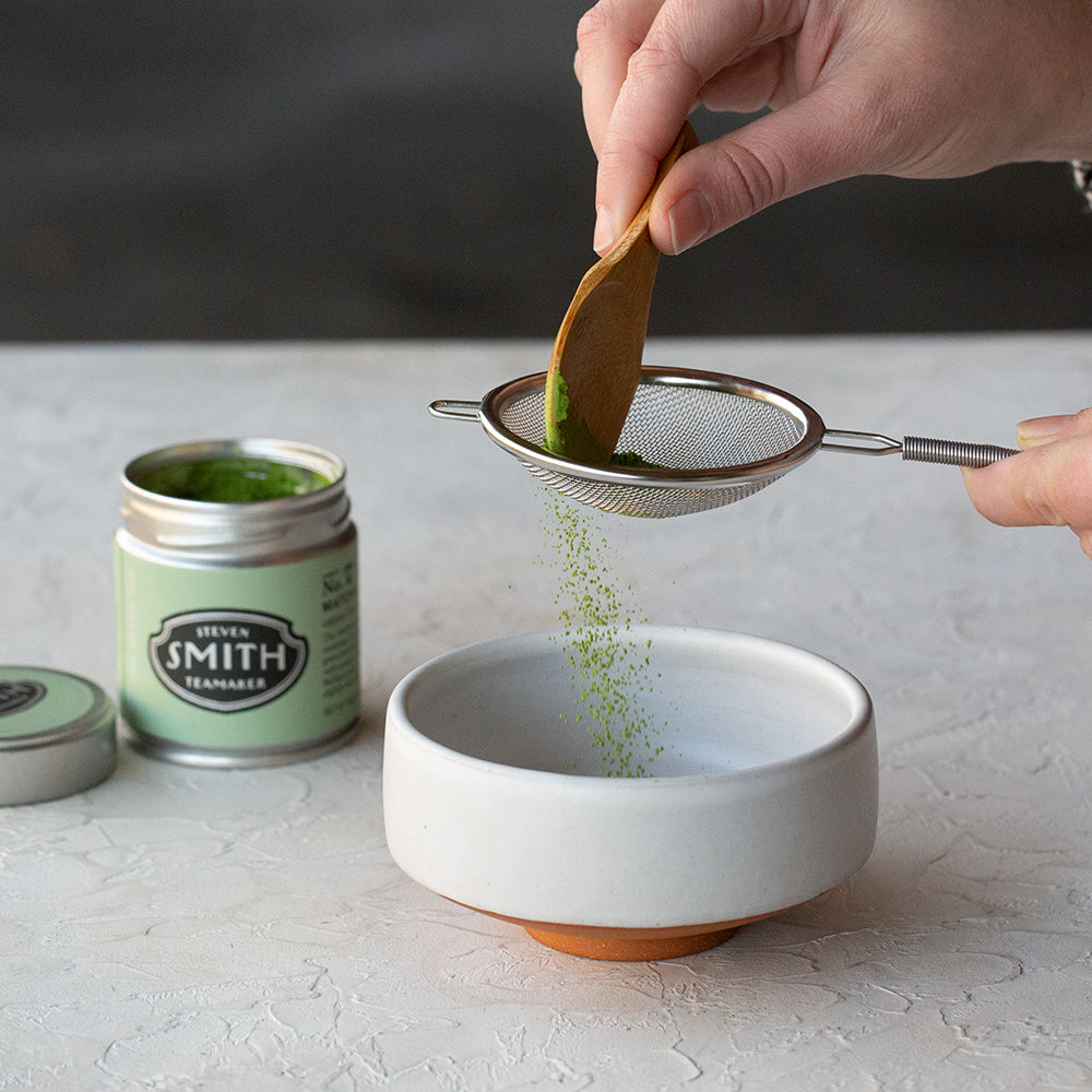 Hand sifting matcha through silver netted sifter.